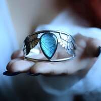 Le souffle de Borée 🪽 

Là où naissent les vents clairs, Borée déploie ses ailes. Elles sont rapides, tranchantes, tissées d’ombre et de lumière froide 💙 

On raconte que Borée naquit d’un éclat d'aube, là où le ciel se déchire pour laisser passer le vent des anciens mondes. Il est le dieu grec du vent du Nord et de l'Hiver, celui qui veille aux confins du monde, celui qui fait vibrer les pins et fait courir les ombres sur la neige ❄️ 

Il est l’esprit qui durcit les eaux, qui aiguise la lumière, qui rend le monde plus clair et plus tranchant.
Il est rude, impétueux et parfois violent. Redoutable et sauvage. Il éprouve, il dépouille, il brise. Il rend à la Terre tout ce qui n’a pas la force de survivre à sa vérité 🪽 

Mais dans son souffle glacial se cache aussi une tendresse ancienne, de celle qui protège, qui purifie, qui resserre l’âme autour de ce qui compte 💙 

Dans chaque hiver, Borée revient. 
Dans chaque vent du nord, son souffle se glisse. Et celui qui écoute vraiment comprend que le froid n’est pas qu'un obstacle, mais aussi une porte. Une invitation à revenir à soi, à la vérité nue, à la force silencieuse que l'on porte en soi. 

Ce bracelet en est son écho. Un talisman forgé pour celles et ceux
qui marchent guidés par le vent du nord 🌬️ 

Une manchette en argent massif 925 entièrement réalisée main par mes soins à l'atelier 🤲🏻 

Deux ailes précieuses qui protègent une incroyable pierre de labradorite bleue au reflet de magie 🪽💙✨ 

Pièce unique disponible demain, le  lundi 8 décembre à 20h pour la sortie de la nouvelle collection ~ La Poésie du Froid ~ 🤍🌬️❄️ 

#cybijoux #hiver #witch #metalsmith #jewellery #sterlingjewelry #winterwitch #artist #witchyvibes #jeweler #jewelry #christmasaesthetic #jewellerydesign #bijouxfaitmain
#silverjewelry #artisanat #faitmain
#artisandefrance #winteraesthetic #hiver #christmasgiftideas #winter #neige #noelaesthetic #wind #christmas #snow
#cadeaufaitmain #noel2025 #greek